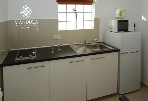 a white kitchen with a sink and a microwave at Mandula Apartman in Cegléd