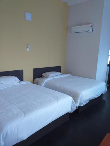 two beds in a hotel room with white sheets at Hotel Peking in Taiping