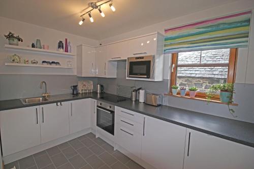 a kitchen with white cabinets and a sink and a window at Six Stevenson House, Oban in Oban