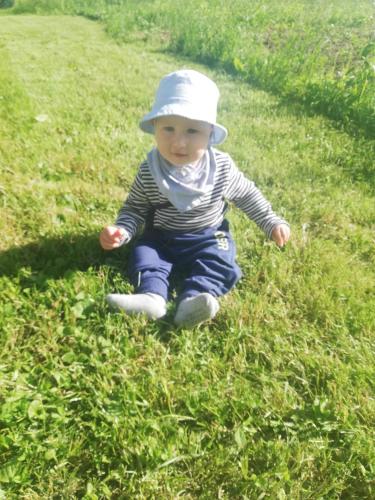a baby wearing a hat sitting in the grass at Grobelnik Tourist Farm in Sevnica