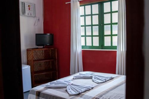a bedroom with a bed with a red wall and a window at Pousada Pelô de Imbassaí in Imbassai