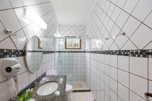 uma casa de banho em azulejos brancos com um lavatório e um espelho. em Recanto da Praia em Paraty