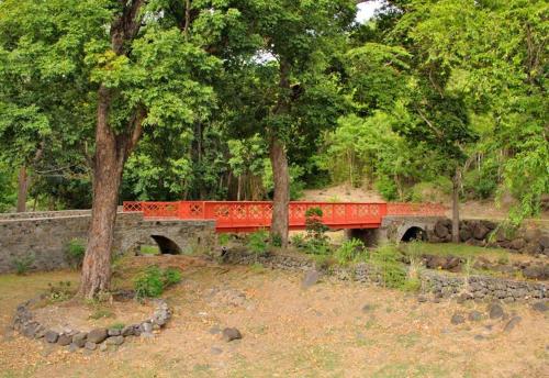a red bridge in the middle of a park with trees at Middle Country 97-1 "la recette du bonheur" in Deshaies