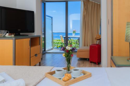 a living room with a television and a table with a vase of flowers at Hotel Savojo in Petrovac na Moru