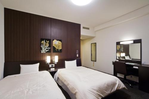 a hotel room with two beds and a desk and a mirror at Hotel Route-Inn Tomakomai Ekimae in Tomakomai