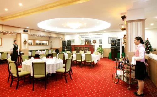 a restaurant with tables and chairs and a woman standing at Sunjin Grand Hotel in Ulaanbaatar