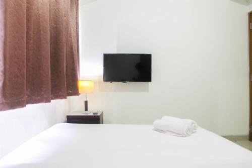 une chambre avec un lit blanc et une télévision à écran plat dans l'établissement 1BR with Working Space The Oasis Cikarang By Travelio, à Cikarang