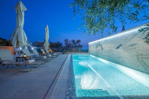 a swimming pool at night with chairs and umbrellas at Villa Stevan in Sveti Stefan