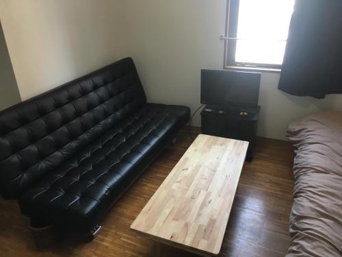 a living room with a black leather couch and a wooden table at コンドミニアムホテル Stay inn Blue 301号室 in Hukue