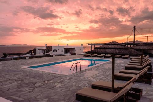 a pool with chairs and an umbrella and the sunset at Sofia's Bungalows Mykonos in Mikonos