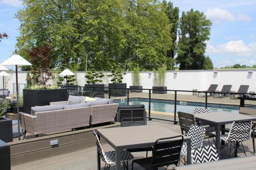 eine Terrasse mit Tischen und Stühlen neben einem Pool in der Unterkunft Golden Tulip Roissy Saint Witz in Saint-Witz