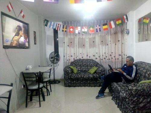 un homme assis sur un canapé dans un salon avec un ordinateur portable dans l'établissement Sunset Hostel Airport, à Lima