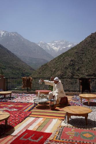 a man sitting on a table with mountains in the background at Berber Family Lodge in Imlil