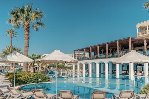 einem Pool mit Stühlen und Sonnenschirmen vor einem Gebäude in der Unterkunft Lindos Imperial Resort & Spa in Kiotari