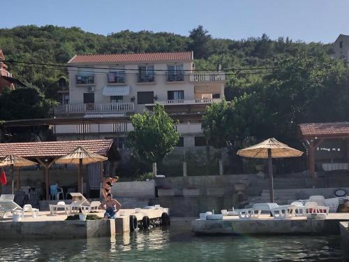 a person sitting on a dock in the water with tables and umbrellas at Apartments Klakor PS in Tivat