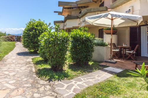 a patio with a table and an umbrella and bushes at Appartamenti Begonia - Terza Spiaggia in Golfo Aranci
