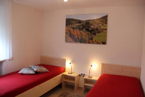 ヴァルメンシュタイナハにあるFerienwohnung Haus am Dürrberg "St. Barbara"のベッドルーム1室(赤いシーツと絵画が備わるベッド2台付)