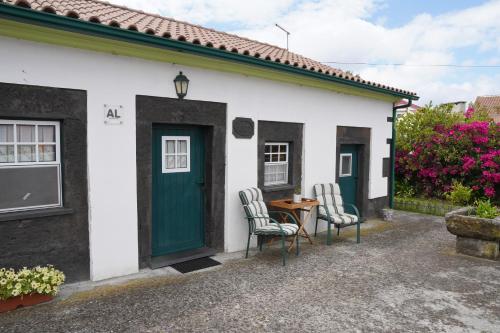 a small white house with a green door and two chairs at Casa do ti' Marrão in Praia da Vitória