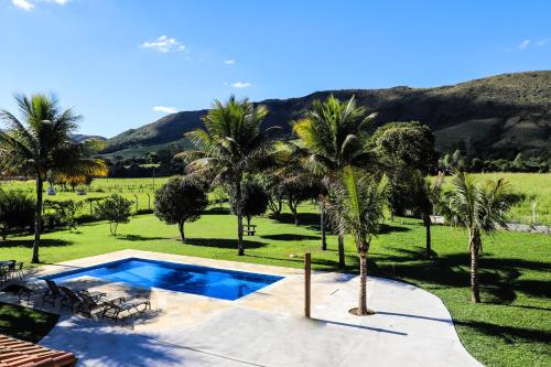 a swimming pool with palm trees and mountains in the background at Pousada Cateto - Zona Rural in Capitólio