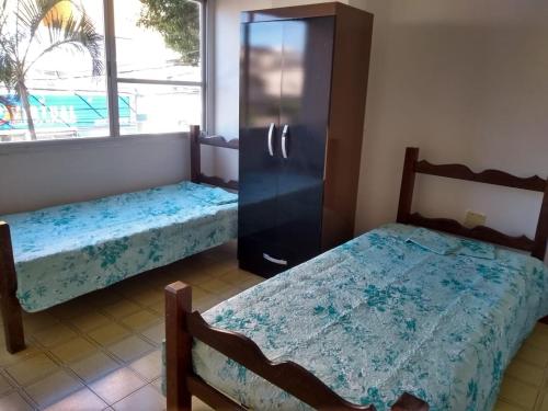 2 Betten in einem Zimmer mit einem Kühlschrank und einem Fenster in der Unterkunft Castanheiras 3 Quartos in Guarapari