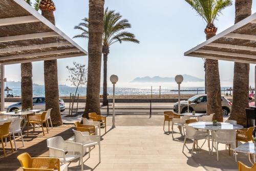 a patio at the beach with tables and chairs and palm trees at Cabot Romantic- Adults Only in Port de Pollensa