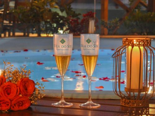 three glasses of wine on a table with a candle at Residencial Vila do Sol, Apartamentos com pé na areia in Bombinhas
