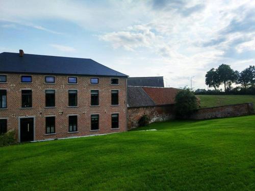 a brick building with a large grassy field next to it at La Maison du Passavant (Gîte à la ferme) in Genappe