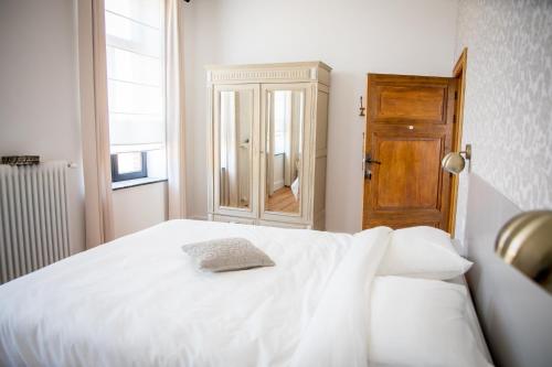 a bedroom with a white bed and a wooden door at La Maison du Passavant (Gîte à la ferme) in Genappe