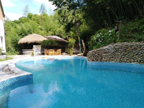 a large blue swimming pool with a stone wall at July Bamboo Hostel in Deqing