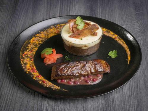 a black plate of food with a dessert on a table at Mercure Bordeaux Aéroport in Mérignac