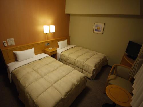 a hotel room with two beds and a chair at Hotel Route-Inn Sakata in Sakata