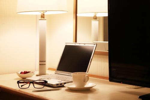 a laptop computer on a desk with a cup and glasses at Hotel Resol Sasebo in Sasebo