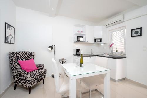 a white kitchen with a table and a chair with a pink pillow at Apartments Roso - ZF Hvar in Hvar