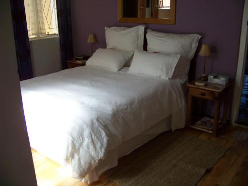 Una cama con sábanas blancas y almohadas en un dormitorio en Lemontree Cottage, en Heidelberg