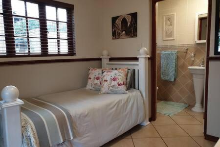 a bedroom with a bed and a bathroom with a sink at The Garden Room in Buffelspoort