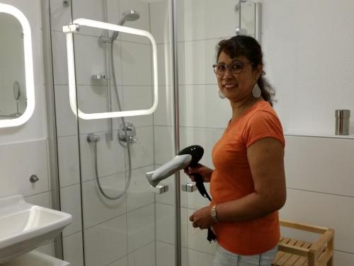 uma mulher de pé numa casa de banho com um secador de cabelo em Ferienwohnung Koralle - Am Wasser em Bremerhaven
