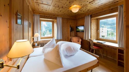 a bedroom with a bed and a lamp and windows at Hotel Bellaval Scuol in Scuol