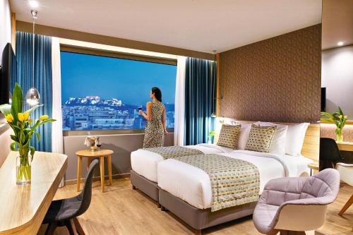a woman standing in a hotel room with a large window at Wyndham Grand Athens in Athens