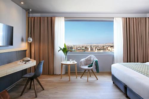 a hotel room with a bed and a desk and a window at Wyndham Grand Athens in Athens