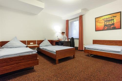 エッセンにあるHotel Böll Essenの三ベッドの部屋の机に座る男