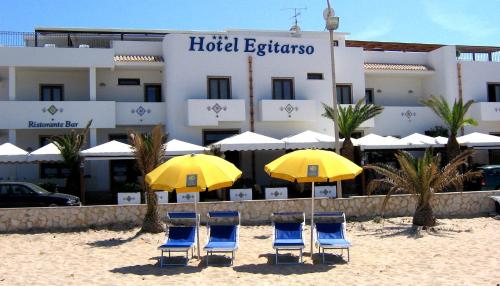 a group of chairs and umbrellas on the beach in front of a hotel at Hotel Egitarso Sul Mare in San Vito lo Capo