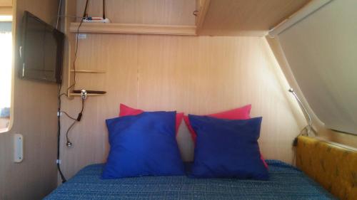 Una cama con almohadas azules y rojas en una habitación pequeña. en Chalet en oasis privado, en La Vegueta