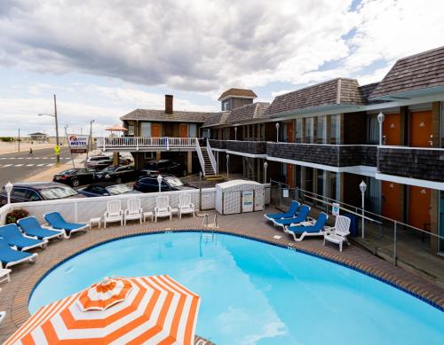a pool in front of a hotel with chairs and an umbrella at Charlroy Motel in Seaside Park