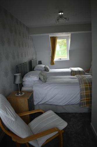 two beds in a room with a chair and a window at Monturpie Guest House in Kirkton of Largo