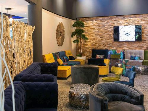 a lobby with couches and chairs and a tv at Mercure Bordeaux Aéroport in Mérignac