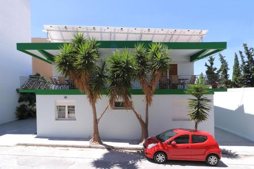 a red car parked next to a building with palm trees at Carpe Diem near the Athens airport in Markopoulo
