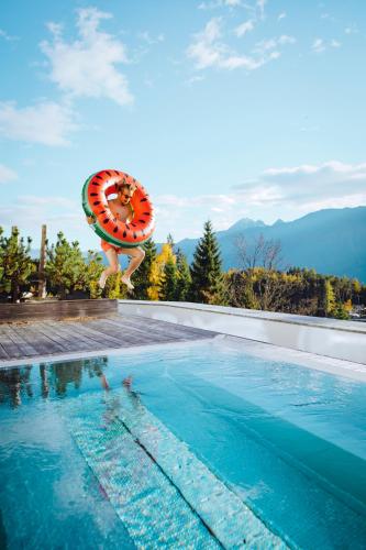 a person jumping into a swimming pool with an umbrella at NIDUM - Casual Luxury Hotel in Seefeld in Tirol