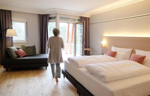 Una mujer caminando por una habitación de hotel con dos camas en Kurhaus Marienkron, en Mönchhof