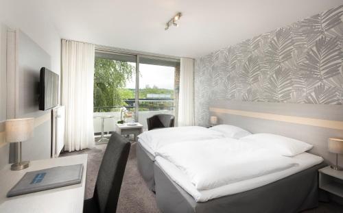 a bedroom with a bed and a desk and a window at Hotel des Nordens Flensburg Wellness & Spa in Flensburg