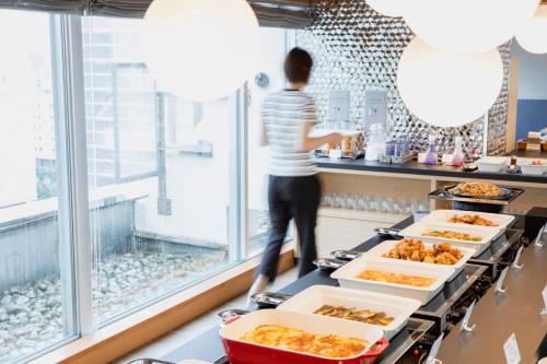 a person standing at a counter looking out the window at food at Hotel Wing International Asahikawa Ekimae in Asahikawa